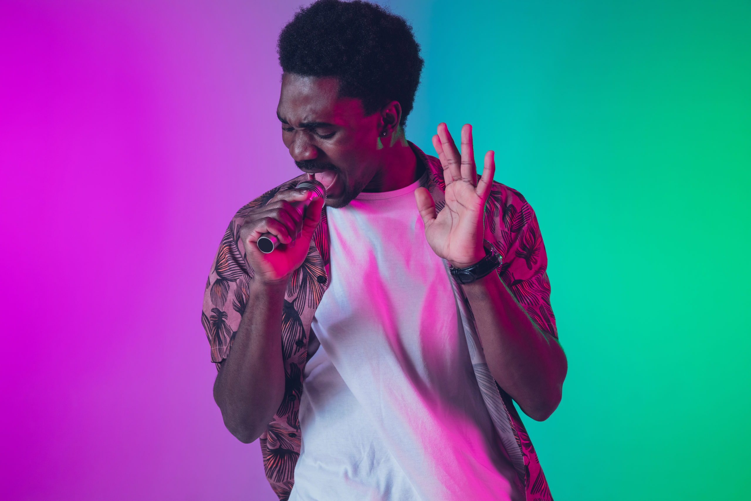 African-american male singer portrait isolated on gradient studio background in neon light. Beautiful male model with microphone. Concept of human emotions, facial expression, ad, music, art.